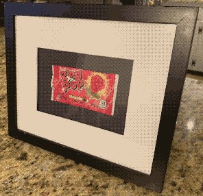 Our engagement Ring Pop wrapper in a wooden frame.